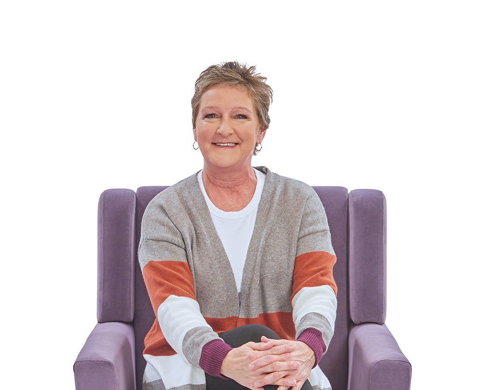 Middle-aged woman sitting in chair smiling.