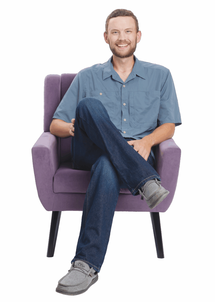 Young man sitting in chair with legs crossed, smiling.